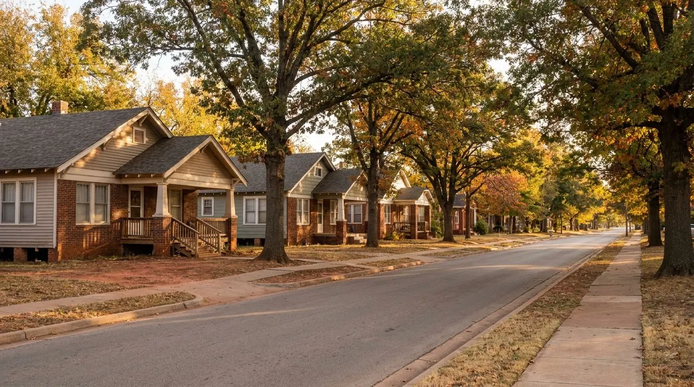 A row of early-1900s wood and brick bungalows with front porches and steps, raised slightly above the ground, under large trees.